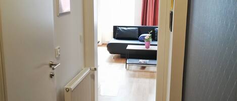 A hallway with a radiator, a black rug, and a clock on the wall.