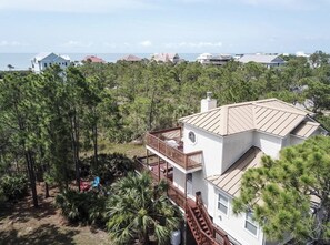 A two-story house with a balcony, surrounded by pine trees and a view of the ocean. - Awesome St George Island Home, Walk to Beach! PET FRIENDLY (St George Island)