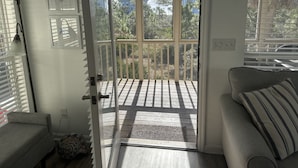 Een kamer met een schuifdeur naar een balkon met een houten terras en uitzicht op bomen en huizen.