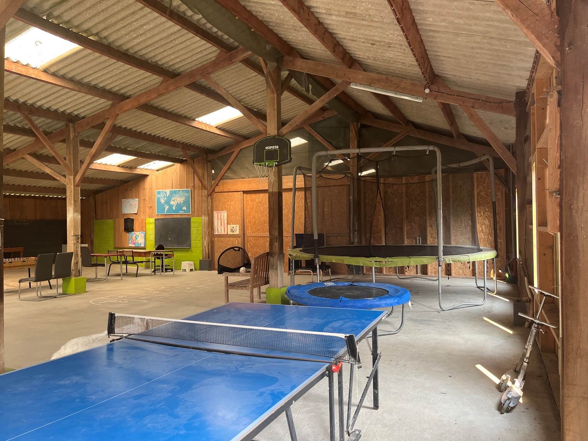 Un espace de loisirs intérieur comprenant des tables de ping-pong, un trampoline et des sièges.