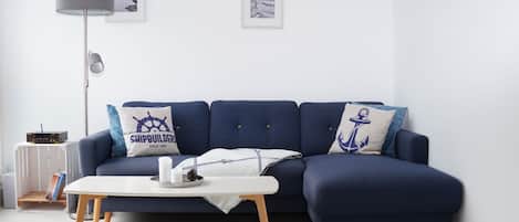 Un salon moderne avec un canapé bleu marine, deux coussins décoratifs, une table basse blanche, un lampadaire et des tableaux encadrés accrochés au mur.