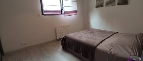 A bedroom with a bed, a window with curtains, a radiator, and a wall with three pictures.