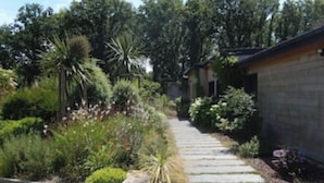 A pathway leading to a building surrounded by lush greenery and various plants. - gite with swimming pool and beach  (Le Tour-du-Parc)