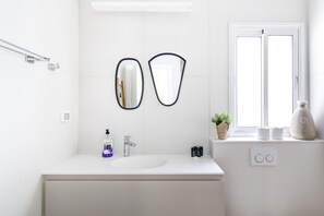 A modern bathroom with a white vanity, a large mirror, a window, and a small plant on the windowsill.