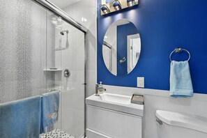 Un baño moderno con cabina de ducha de vidrio, lavamanos blanco y pared azul.