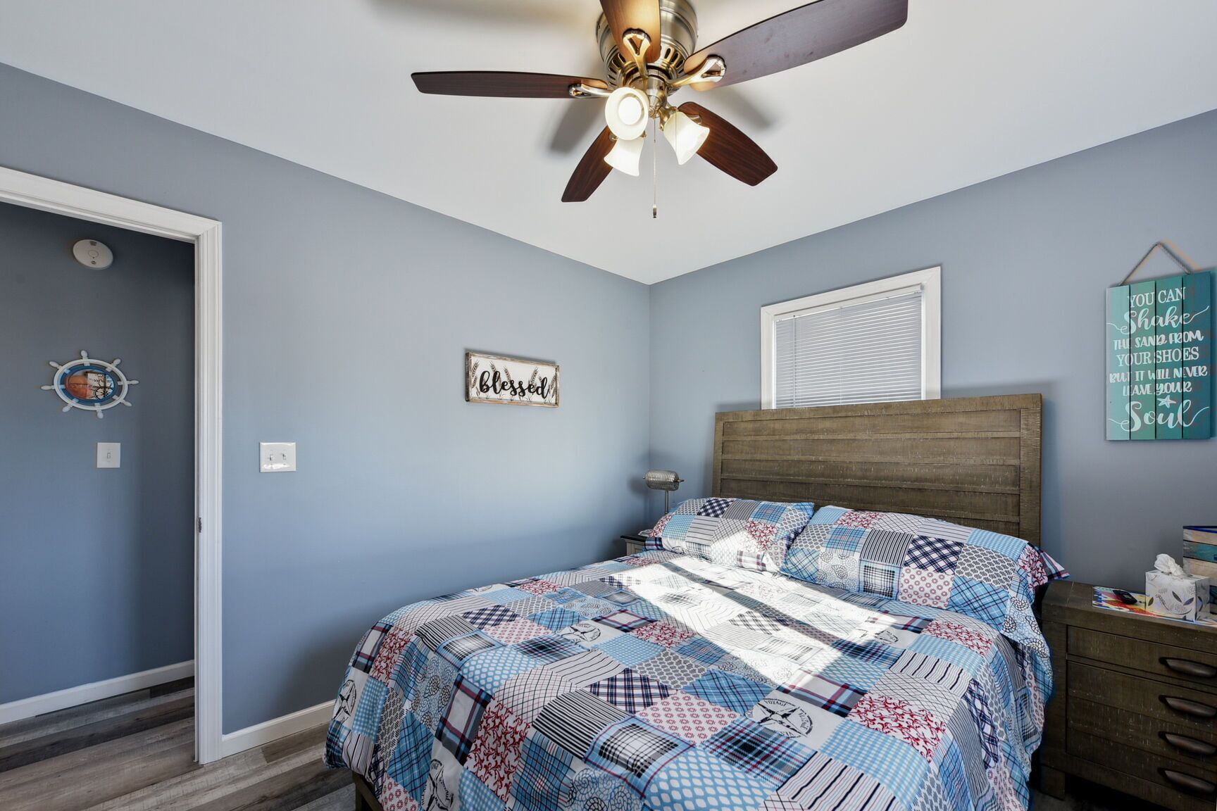 A bedroom with a bed, a ceiling fan, a wall clock, a window, and a wall decoration.