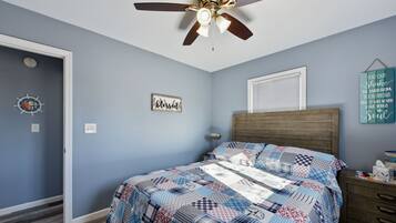 A bedroom with a bed, a ceiling fan, a wall clock, a window, and a wall decoration.