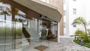 A modern building entrance with glass doors, a concrete overhang, and a paved pathway leading to a staircase. - Serena Apartment with Terrace and Golf View (motril)
