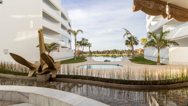 A modern hotel with a pool area, palm trees, and a clear sky. - Serena Apartment with Terrace and Golf View (motril)