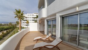 A modern balcony with two lounge chairs, a wooden floor, and a view of a white building and palm trees. - Serena Apartment with Terrace and Golf View (motril)