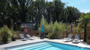 A rectangular swimming pool with a wooden deck, surrounded by lounge chairs and umbrellas.