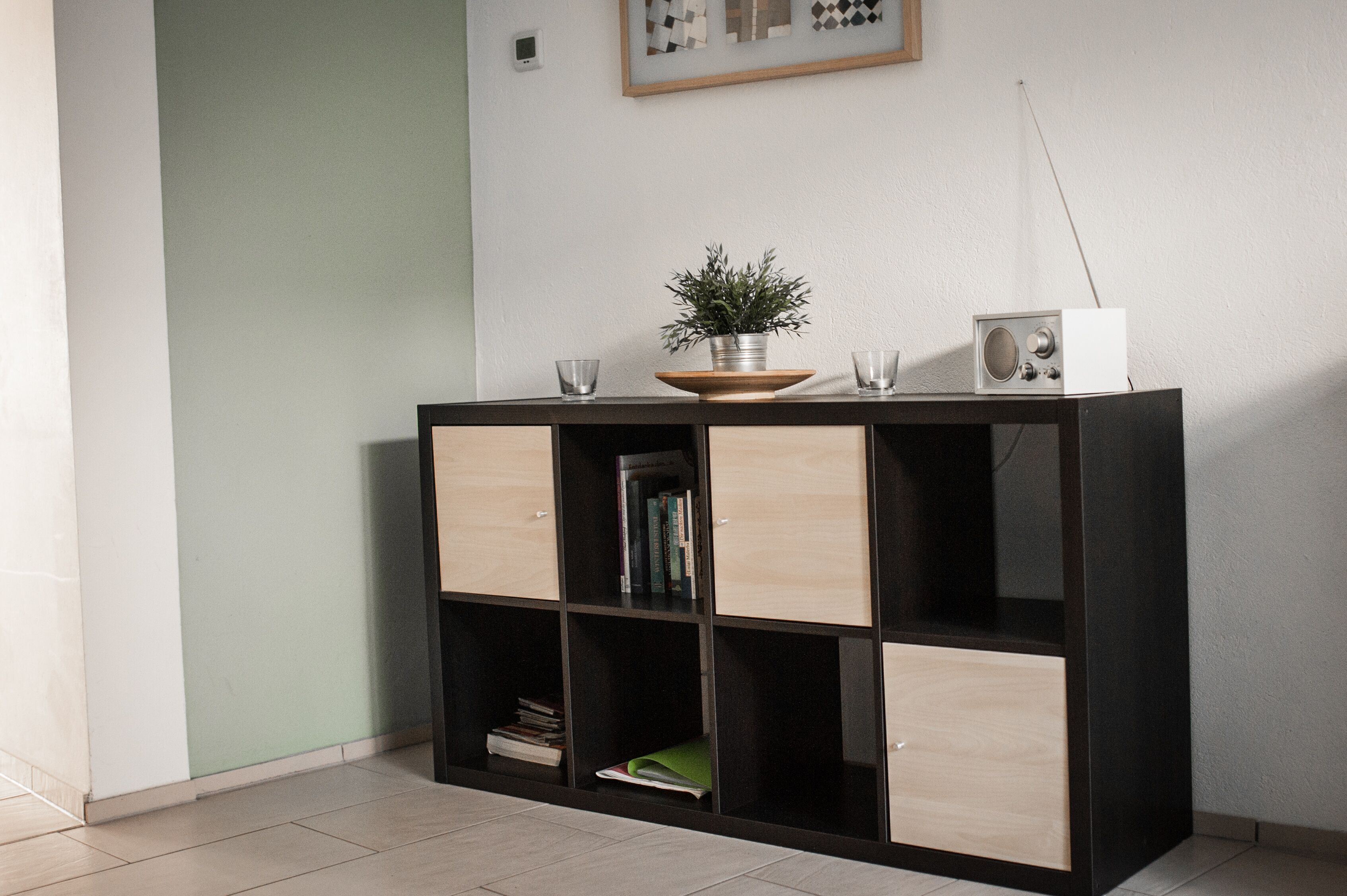 A modern, minimalist room with a black and light wood cabinet, a small potted plant, and a vintage radio on top.