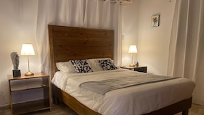 A neatly made bed with a wooden headboard, two bedside tables with lamps, and a small shelf. - Caribbean Golf (Punta Cana)