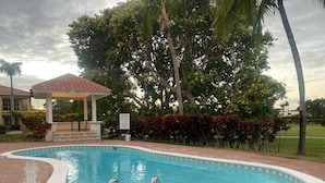 A swimming pool with a curved edge, a gazebo, and a signboard. - Caribbean Golf (Punta Cana)