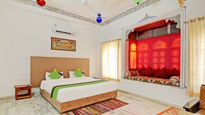 A hotel room with a bed, a small bedside table, a window with red curtains, a ceiling fan, and an air conditioning unit. - Treebo Khakhri Haveli (Udaipur)