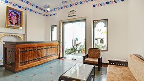 A reception area with a wooden desk, a sofa, and a chair. There is a large window with a view of the outside. - Treebo Khakhri Haveli (Udaipur)