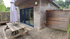 A wooden cabin with a sliding glass door, a picnic table, and an umbrella. - Nice cottage with swimming pool, 5 min from the beach, called "STIBIDEN". (Le Tour-du-Parc)