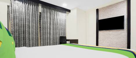 Habitación de hotel con cama, televisor montado en la pared, ventilador de techo y ventana con cortinas.