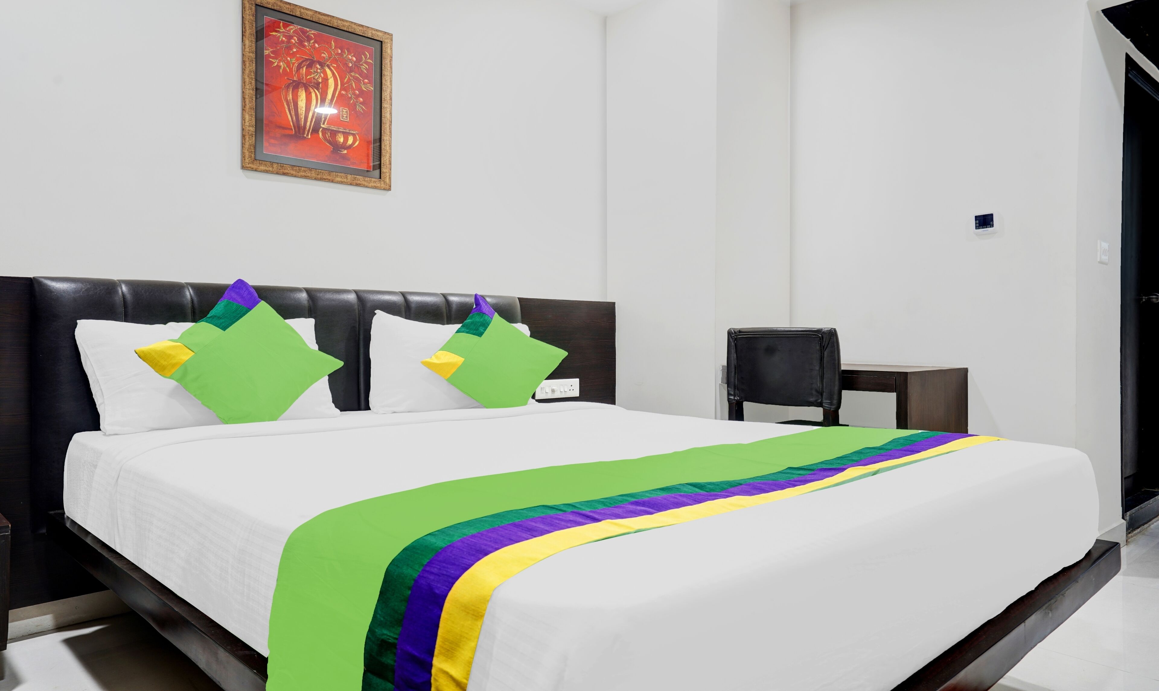 A hotel room with a black headboard, white bedding, and a colorful bedspread.
