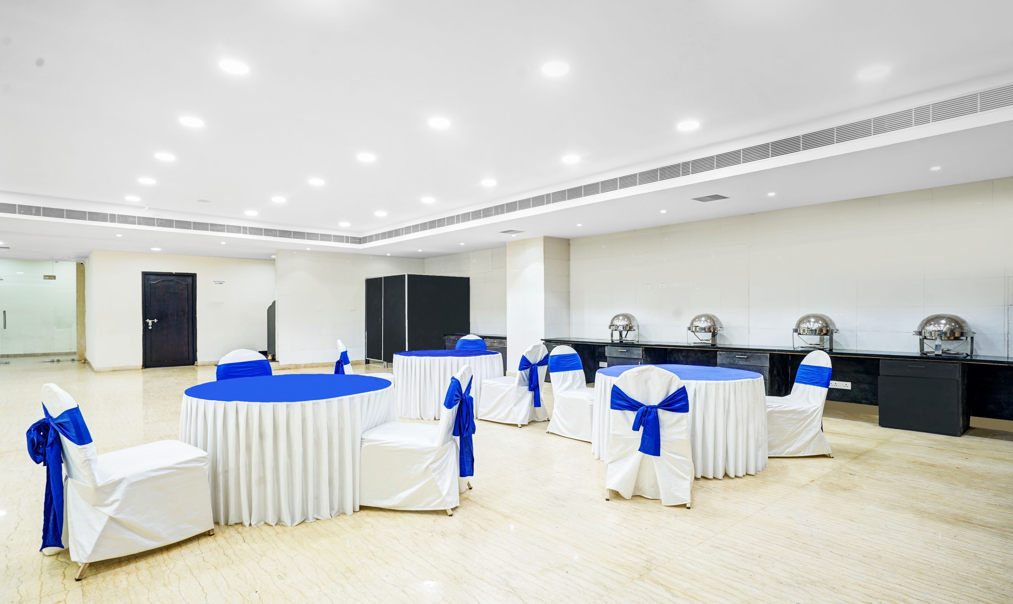 A conference room with round tables, white chairs with blue sashes, a black reception desk, and a tiled wall.