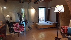 A bedroom with a bed, a chair, a lamp, and a view of the outdoors.