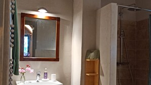 A bathroom with a wooden shelf, a mirror, a sink, and a shower.