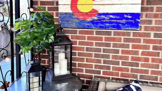 Eine rustikale Backsteinmauer mit bemaltem Colorado-Staatswappen, einem schwarzen Laternen und einem Blumentopf.