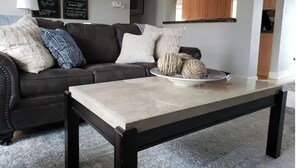Ein Wohnzimmer mit einem dunkelbraunen Ledersofa, einem Couchtisch mit einer dekorativen Schale und einer durch einen Bogen sichtbaren Küche.