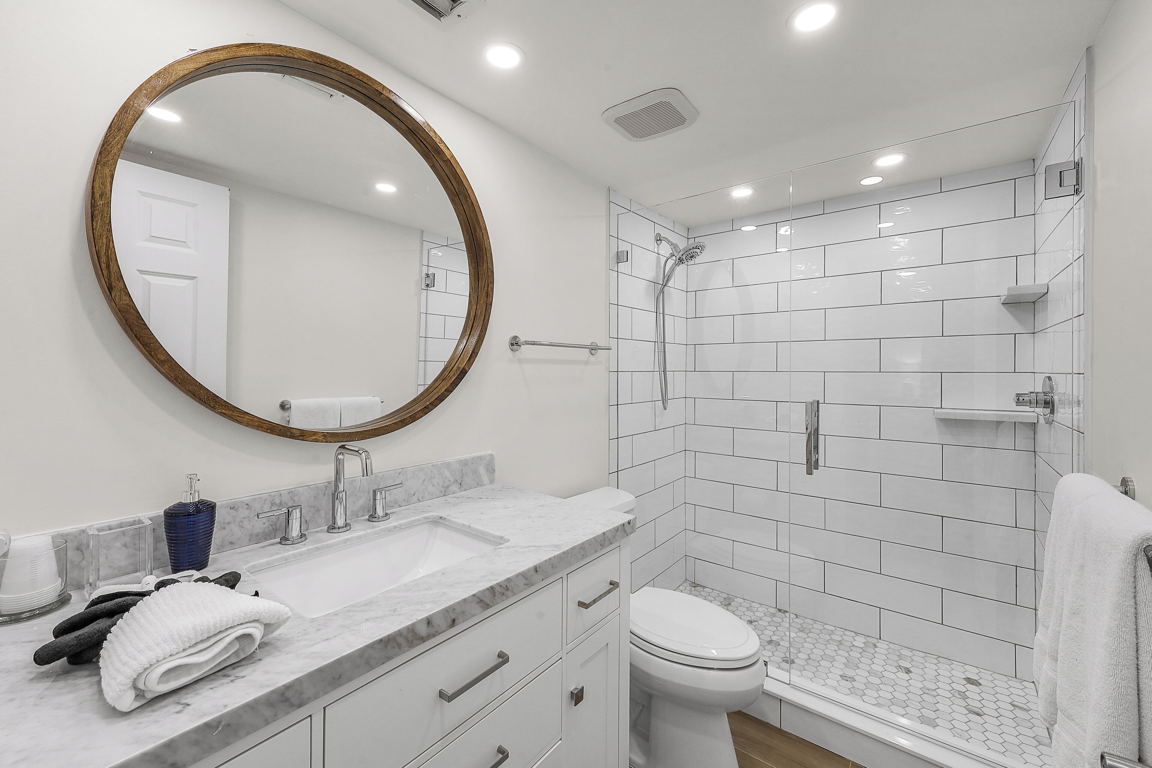A modern bathroom with a marble sink, a large mirror, a toilet, and a shower area.