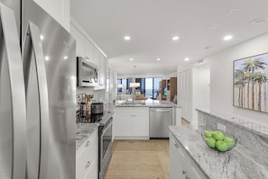 A modern kitchen with stainless steel appliances, white cabinetry, and a granite countertop. - Beachfront Condo | Pool, Gym, & Pickleball (Marco Island)