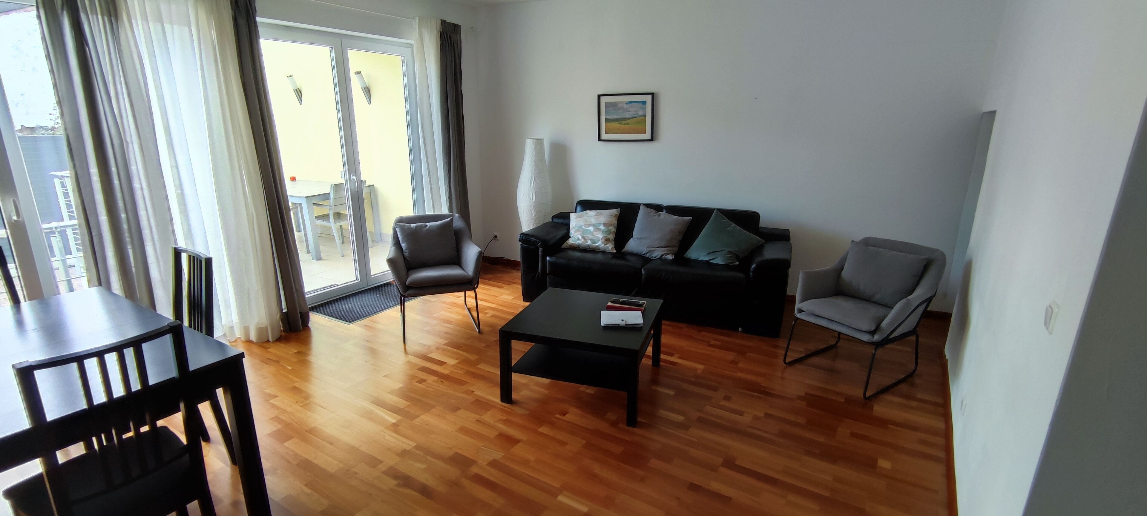 Ein Wohnzimmer mit Holzboden, einer schwarzen Couch mit Kissen, einem schwarzen Couchtisch und einem grauen Sessel.