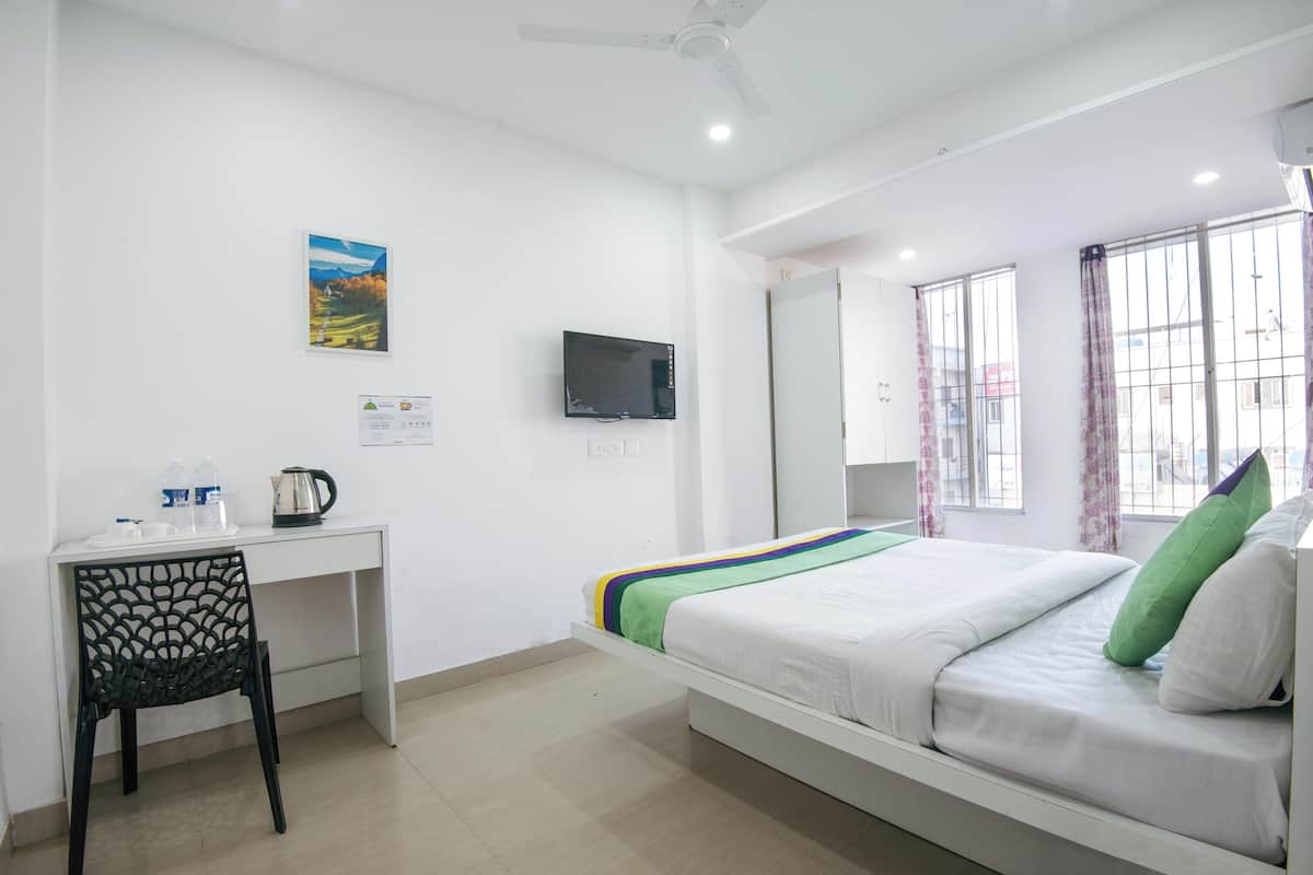 A hotel room with a bed, a desk, a chair, a TV, and a window with curtains.