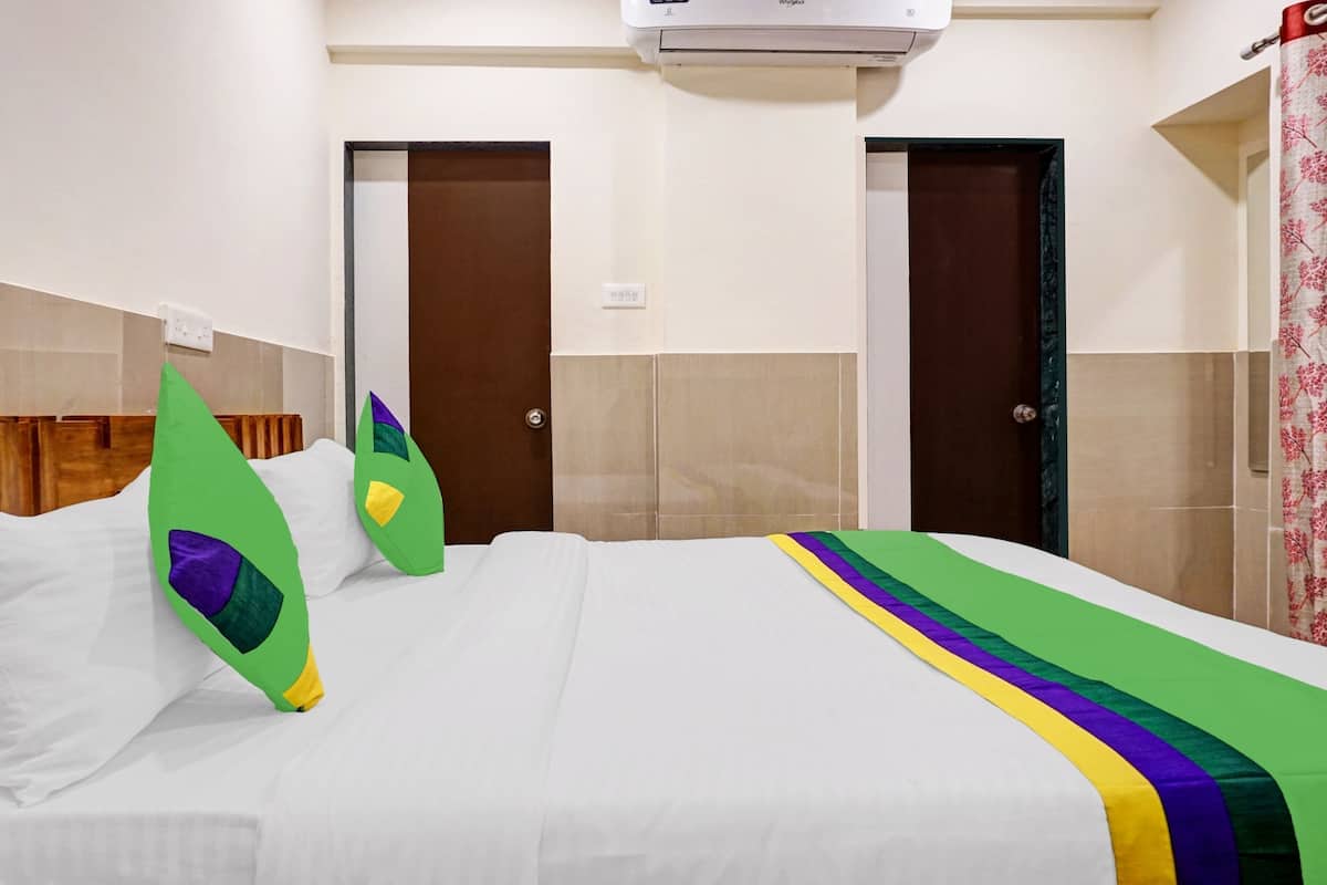 A hotel room with a bed, two doors, an air conditioning unit, and a power outlet.