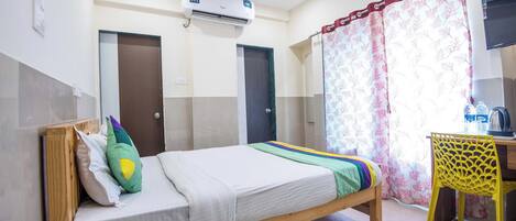 A hotel room with a bed, a desk, a chair, an air conditioner, and a curtain.