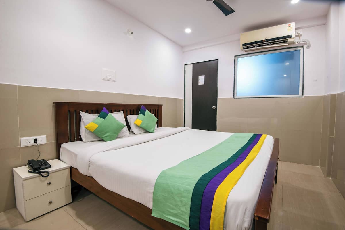 A neatly made bed with a rainbow-striped blanket, a bedside phone, and a window with a view.