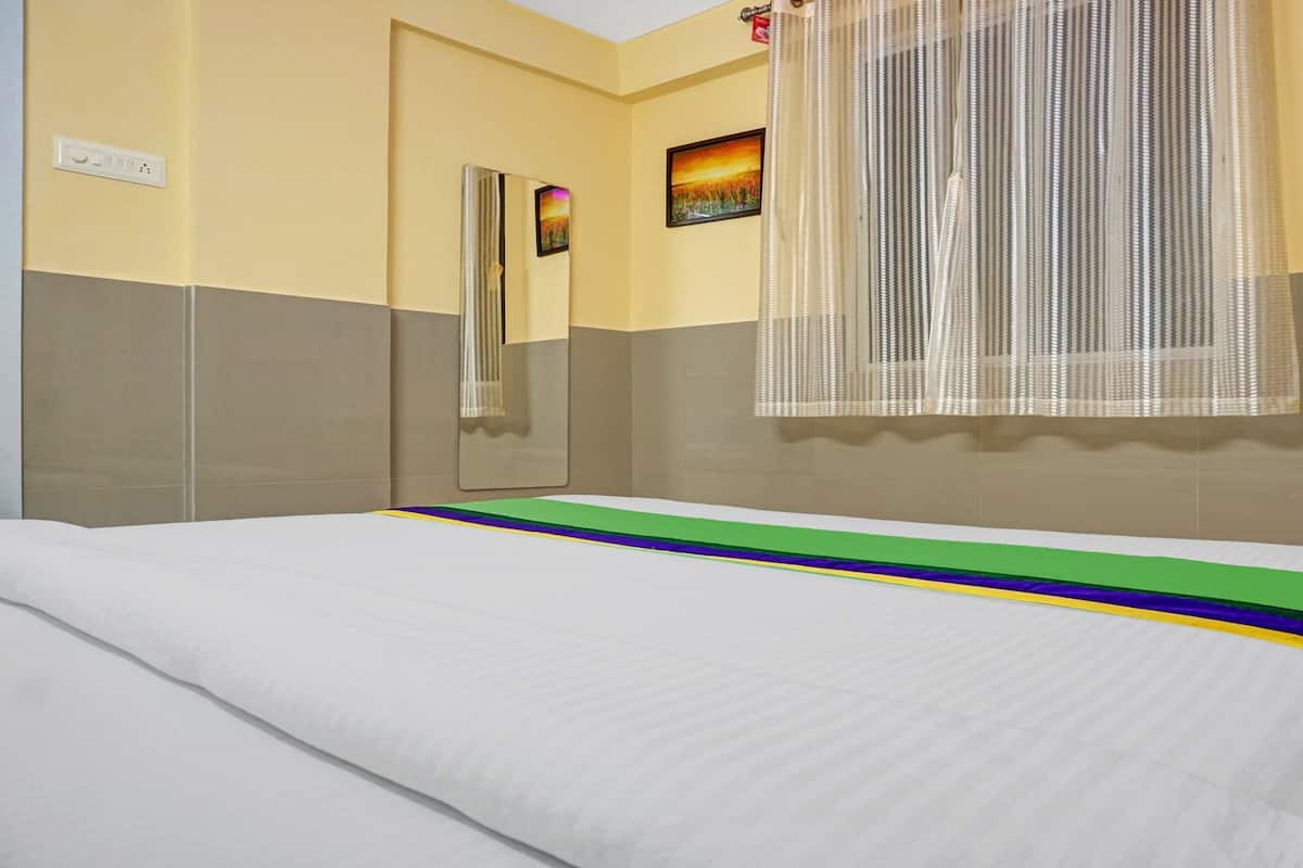 A hotel room with a bed, a wall-mounted mirror, a painting, and a window with a sheer curtain.