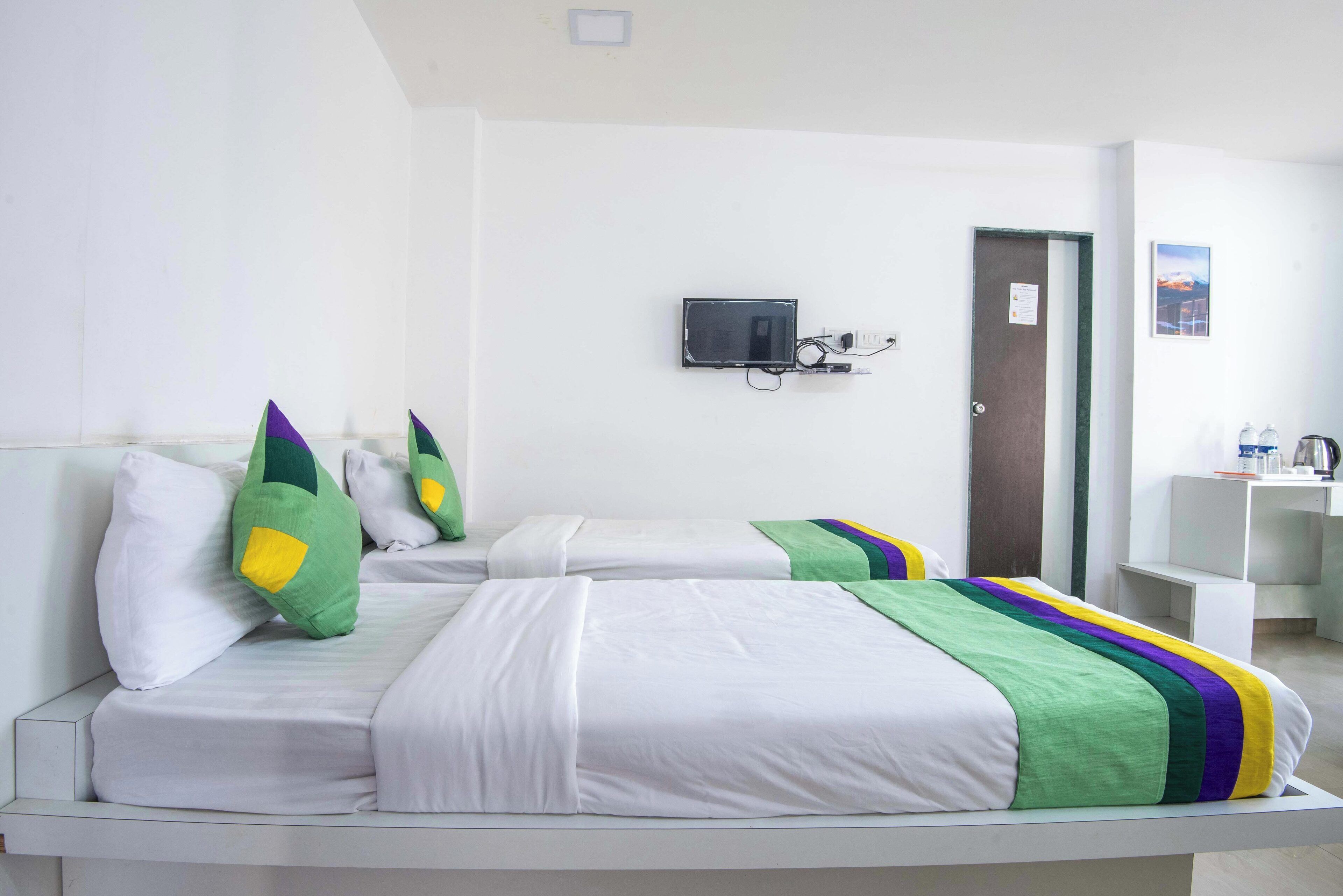 A hotel room with two beds, a TV mounted on the wall, a door, and a small desk with a sink.