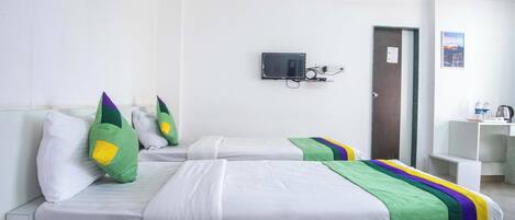 A hotel room with two beds, a TV mounted on the wall, a door, and a small desk with a sink.
