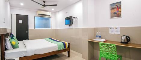 Ein Hotelzimmer mit Bett, Schreibtisch, Stuhl, Deckenventilator, Klimaanlage und einem Bild an der Wand.