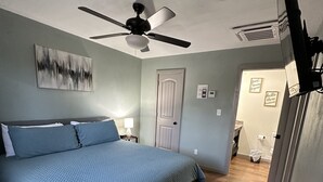 Ein Schlafzimmer mit Bett, Deckenventilator, Tür und Wand-Fernseher.