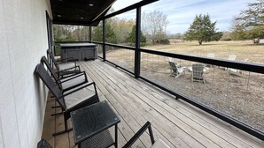 Eine überdachte Terrasse im Freien mit Whirlpool, Sitzgelegenheit und Blick auf eine Wiese.