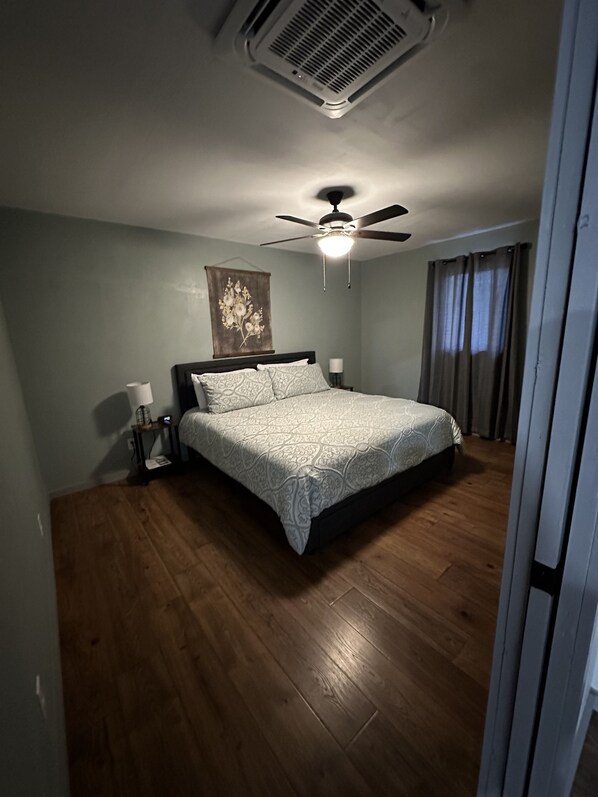 Une chambre à coucher avec un lit, un ventilateur de plafond, un climatiseur fixé au mur et une fenêtre avec des rideaux.