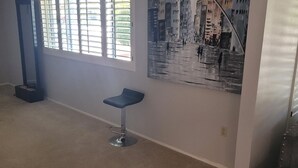A spacious living room with a large window, a modern bar stool, and a cityscape painting on the wall. - Nice home for rent in a quiet area close to Scottsdale and Glendale  area.  Open (Sun City)
