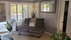 A living room with a grey sofa, a patterned throw pillow, a potted plant, and a large mirror on the wall. - Nice home for rent in a quiet area close to Scottsdale and Glendale  area.  Open (Sun City)