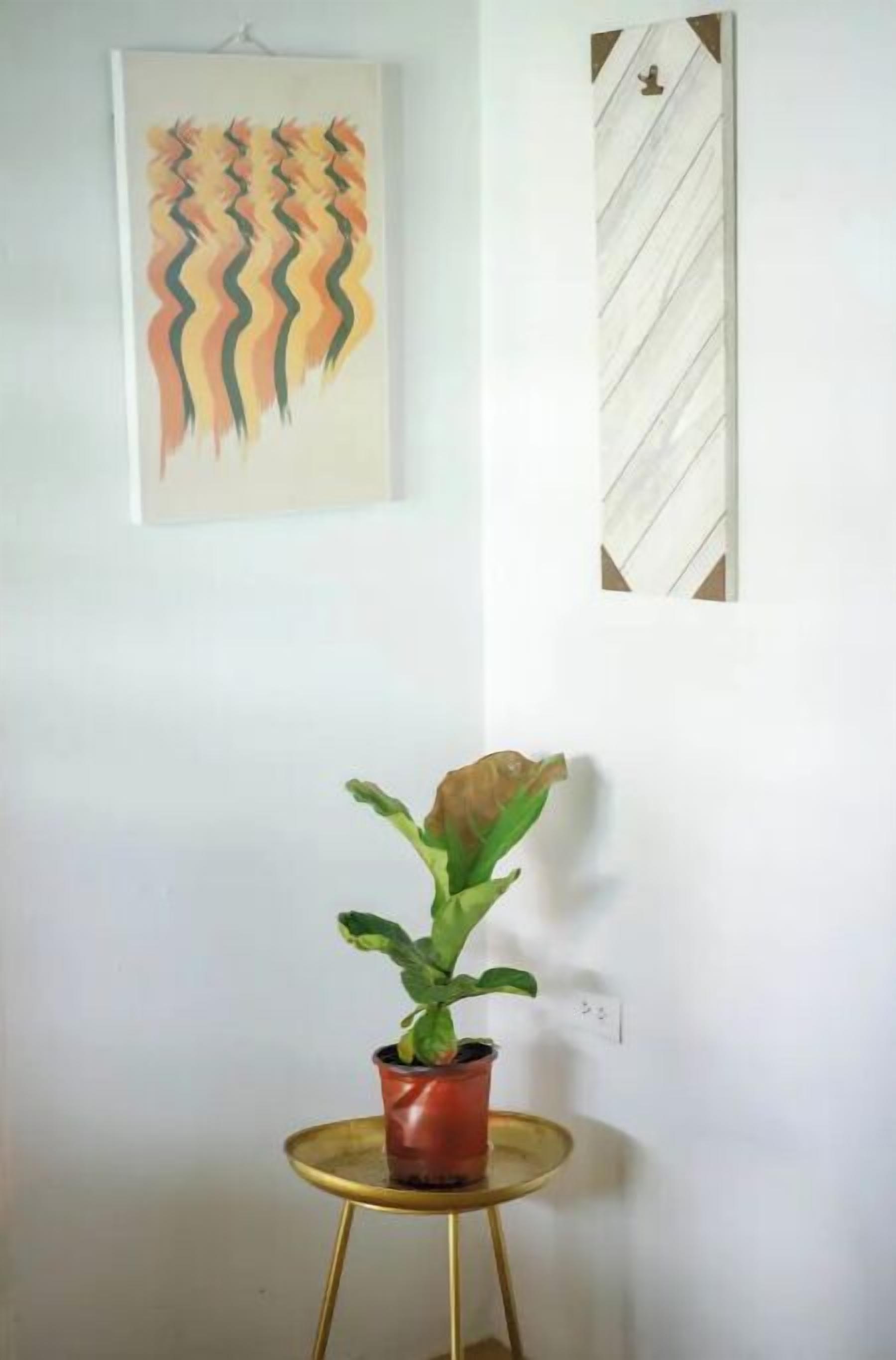 Une pièce avec une plante en pot sur une petite table ronde, un tableau au mur et un panneau décoratif.