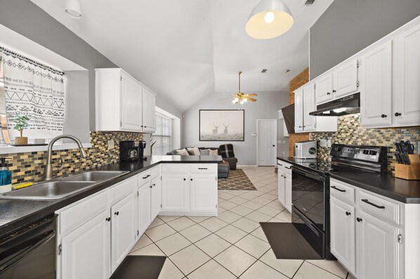A modern kitchen with white cabinets, black countertops, and a tiled backsplash.