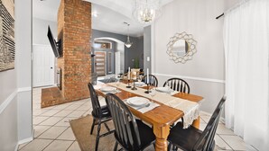 A dining area with a brick wall, a chandelier, and a white curtain. - Texas Oasis With Pool! (Fort Worth)