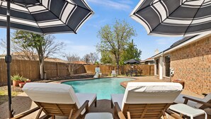 A backyard with a swimming pool, wooden lounge chairs, and umbrellas. - Texas Oasis With Pool! (Fort Worth)