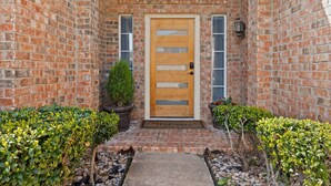 A brick building with a wooden door, potted plants, and a welcome mat. - Texas Oasis With Pool! (Fort Worth)