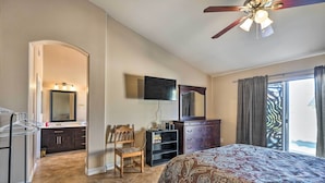 Une chambre à coucher avec un lit, un ventilateur de plafond, une télévision, une commode et une fenêtre avec des rideaux.